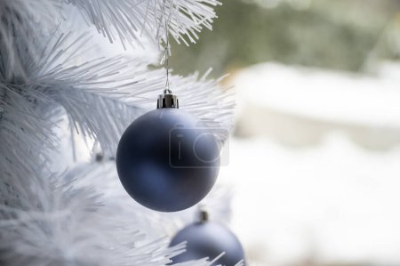 Foto de Vista de cerca de la bola de navidad azul liso colgando de un árbol de vacaciones blanco. - Imagen libre de derechos