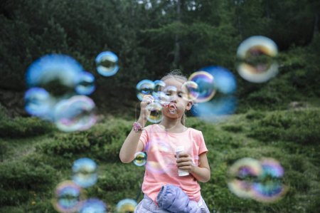 Foto de Niña soplando burbujas de jabón en la hermosa naturaleza verde de verano. - Imagen libre de derechos