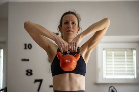 Foto de Ajuste mujer joven haciendo ejercicio en casa levantando un peso kettlebell 8kg. - Imagen libre de derechos