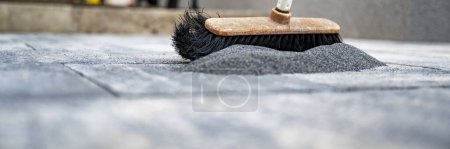 Foto de Vista de ángulo bajo de una escoba cepillando arena especial entre las baldosas de cemento recién layed en un patio al aire libre o acera. - Imagen libre de derechos