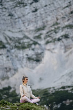 Foto de Mujer joven sentada en una posición de loto en una roca en las altas montañas meditando y practicando mindfulness. - Imagen libre de derechos