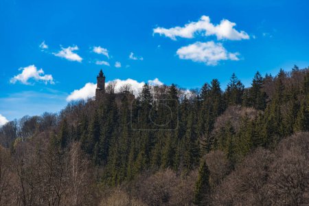 Foto de Zagorze Slaskie, Polonia - Abril 2022: Colina llena de árboles sin hojas con un castillo de Grodno en la colina y el cielo es azul con unas pequeñas nubes - Imagen libre de derechos