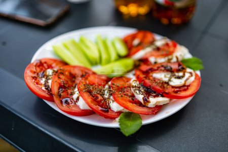 Téléchargez les photos : Assiette blanche pleine de tranches de concombre et de tomates et de fromage mozzarella comme salade capreze - en image libre de droit