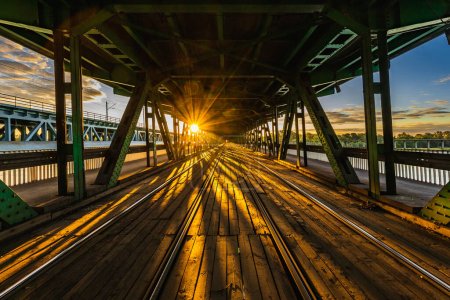 Foto de Varsovia, Polonia - Julio 2022: Puente largo de madera y metal Gdanski con rieles de tranvía y techo verde visto por la mañana al amanecer hora dorada - Imagen libre de derechos