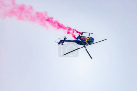 Photo for Leszno, Poland - June 16 2023: Antidotum Airshow Leszno 2023 and acrobatic shows full of smoke of Felix Baumgartner flying by helicopter Red Bull Bo 105 on a cloudy sky - Royalty Free Image