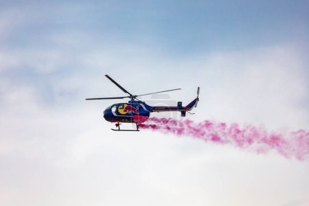 Photo for Leszno, Poland - June 16 2023: Antidotum Airshow Leszno 2023 and acrobatic shows full of smoke of Felix Baumgartner flying by helicopter Red Bull Bo 105 on a cloudy sky - Royalty Free Image