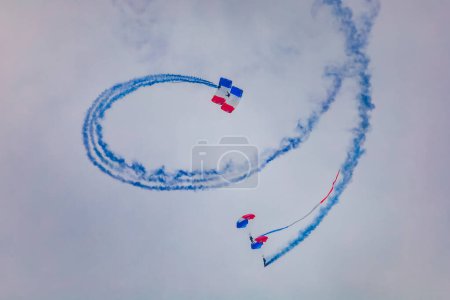 Photo for Leszno, Poland - June 17 2023: Antidotum Airshow Leszno 2023 and show of PHENIX Ambassadeurs Parachutistes flying down on parachutes with french and polish flag and a lot of smoke - Royalty Free Image