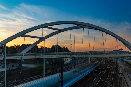 Photo for Gdansk, Poland - September 7 2023: Beautiful and colorful cloudy sunset at golden hour with golden and blue sky seen from small footbridge over train rails with driving trains - Royalty Free Image