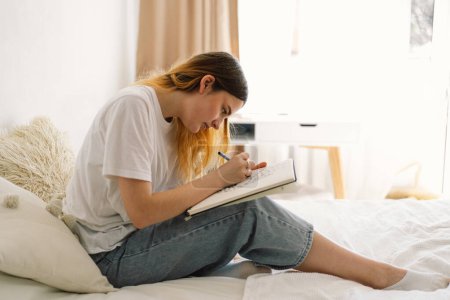 Foto de Una adolescente está dibujando o haciendo deberes en el dormitorio. Un adolescente estudia en casa. Regreso a la escuela - Imagen libre de derechos
