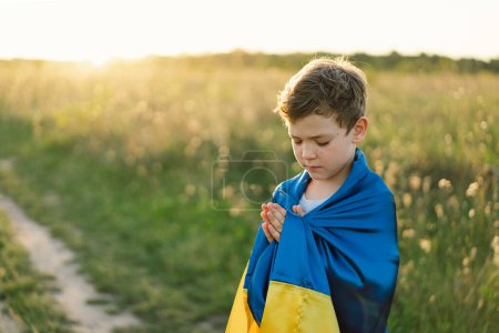 Ukrainian boy closed her eyes and praying to stop the war in Ukraine in a field at sunset. Hands folded in prayer concept for faith, spirituality and religion. War of Russia against Ukraine. Stop War