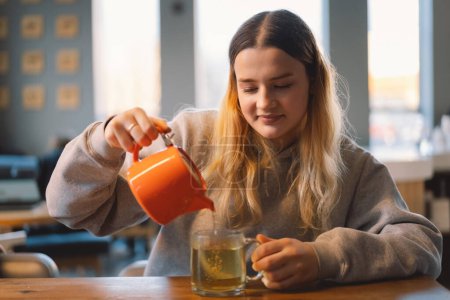 Photo for Portrait of a joyful teengirl enjoying a cup of tea at cafe. Smiling beautiful girl drinks hot tea in winter. Teengirl drinking hot tea. Cafe city lifestyle. Colorful portrait of happy pretty girl - Royalty Free Image