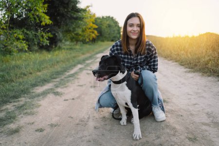Photo for Human and a dog. Teengirl and her friend staffer dog on the field background. Beautiful young woman relaxed and carefree enjoying a summer sunset with her lovely dog. Lifestyle - Royalty Free Image