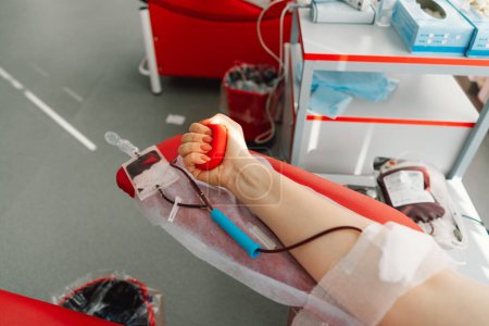 Foto de Mujer joven haciendo donación de sangre en el hospital. Una mujer dona sangre mientras sostiene un corazón rojo. Donación de sangre. - Imagen libre de derechos