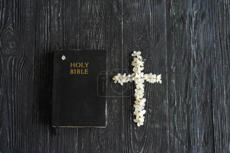 Frühlingsblumen in Form eines Kreuzes mit einer Bibel auf altem Holzgrund. Ostern ist ein christlicher Feiertag