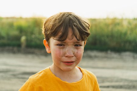 Porträt eines Jungen in der Natur. Ein Junge im orangefarbenen T-Shirt weint in der Natur. Nicht-positives Kind, Lebensstil.