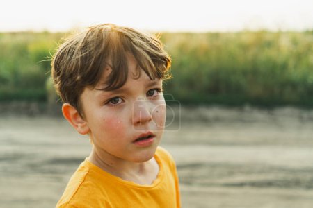 Portrait d'un garçon dans la nature. Un garçon en T-shirt orange pleure dans la nature. Enfant non positif, mode de vie.
