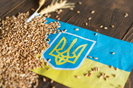 Wheat grains with yellow and blue Ukrainian flag on wooden background. Export, sale, import of Ukrainian grain. Ukrainian grain.