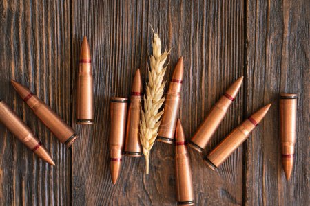 Wheat grains are spread across a wooden table, interspersed with several metal bullet shells. The concept of the photo suggests that grain can be used as a weapon. Hunger as a weapon against humanity