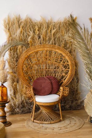 A cozy corner features a vintage-inspired rattan peacock chair adorned with a soft white cushion and a burgundy throw pillow.