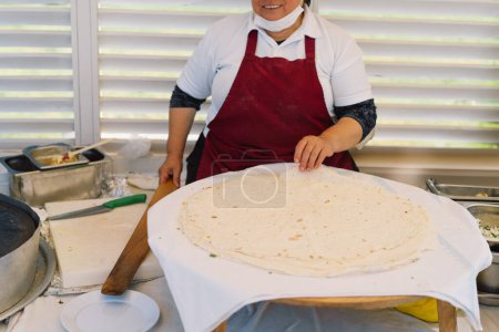 Téléchargez les photos : Une femme qui prépare un gros morceau de pain plat. Elle travaille sur un stand de marché extérieur, entouré d'ustensiles de cuisine et d'ingrédients, présentant un aperçu des pratiques culinaires locales.. - en image libre de droit