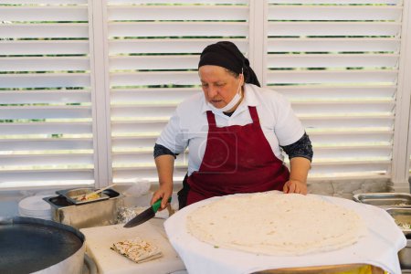 Une femme qui prépare un gros morceau de pain plat. Elle travaille sur un stand de marché extérieur, entouré d'ustensiles de cuisine et d'ingrédients, présentant un aperçu des pratiques culinaires locales..