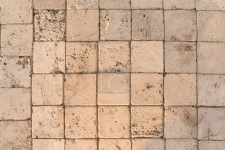 The detail of worn stone paving blocks, showcasing their texture and the subtle color variations due to weathering. The natural light enhances the stones sandy tones