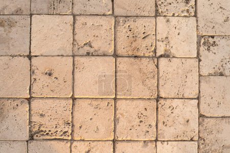 The detail of worn stone paving blocks, showcasing their texture and the subtle color variations due to weathering. The natural light enhances the stones sandy tones