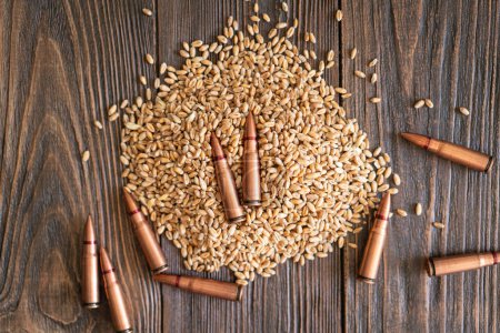 Wheat grains are spread across a wooden table, interspersed with several metal bullet shells. The concept of the photo suggests that grain can be used as a weapon. Hunger as a weapon against humanity