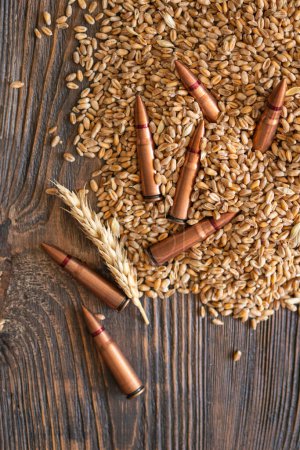 Los granos de trigo se extienden a través de una mesa de madera, intercalados con varias balas metálicas. El concepto de la foto sugiere que el grano se puede utilizar como arma. El hambre como arma contra la humanidad