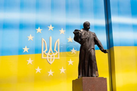 La estatua de una figura ucraniana excepcional Taras Shevchenko se encuentra en el fondo de una brillante bandera ucraniana. Clima soleado brillante mejora el atractivo visual de la escena.