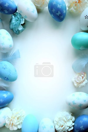 Foto de Concepto de decoraciones de Pascua. Foto de vista superior de huevos de Pascua coloridos, flores y plumas azules sobre fondo azul pastel aislado. - Imagen libre de derechos