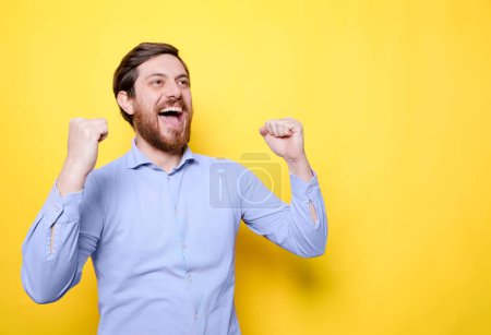 Happy man celebrating success with clenched fists on yellow background