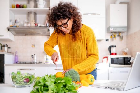 Téléchargez les photos : Cheerful black woman learning to cook at home watching online tutorial - en image libre de droit