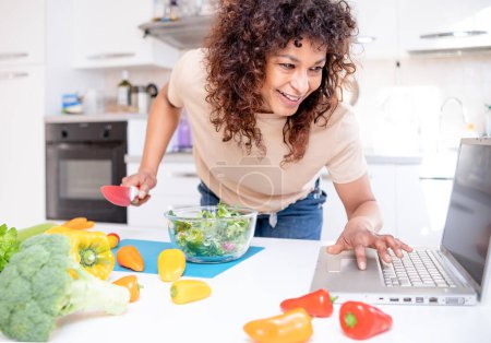 Photo for Happy black woman learning to cook at home with online courses - Royalty Free Image