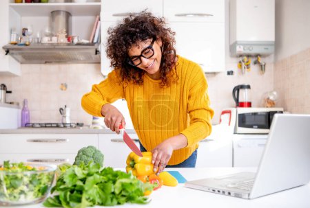 Photo for Cheerful black woman learning to cook at home watching online tutorial - Royalty Free Image