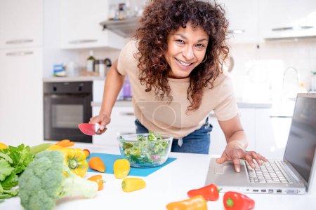Photo for Cheerful black woman learning to cook at home watching online tutorial - Royalty Free Image