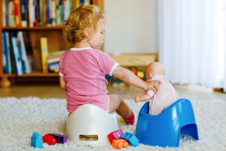 Primer plano de un niño pequeño y lindo de 12 meses sentado en el orinal. Niño jugando con muñeco de juguete. Concepto de entrenamiento de baño. Aprendizaje del bebé, pasos de desarrollo.