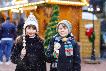 Photo for Little cute kid girl and boy eating white chocolate covered strawberries and apple on skewer on traditional German Christmas market. Happy children, best friends, twins and siblings on snowy day. - Royalty Free Image