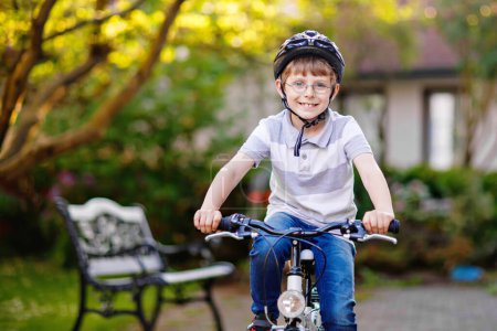 Téléchargez les photos : Joyeux garçon de l'école qui s'amuse avec le vélo. Enfant actif avec casque de sécurité faisant du sport avec vélo dans la nature. Concept sécurité, sport, loisirs avec enfants
. - en image libre de droit