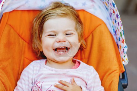 Téléchargez les photos : Portrait de petite fille tout-petit souriante et mignonne assise dans une poussette ou un landau et allant se promener. Joyeux bébé enfant mignon qui s'amuse à l'extérieur. Fille saine - en image libre de droit