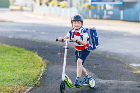 Photo for Active school kid boy in safety helmet riding with his scooter in the city with backpack on sunny day. Happy child biking on way to school. Safe way for kids outdoors to school - Royalty Free Image