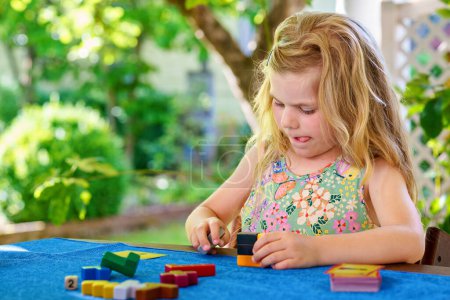 Téléchargez les photos : Little preschool girl playing board game with colorful bricks. Happy child build tower of wooden blocks, developing fine motor skills, home joint games. Leisure activities for children at home - en image libre de droit