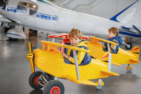 Photo for Two little kids boysy driving big toy old vintage pedal plane and having fun, indoors. Active leisure with children during school holidays - Royalty Free Image