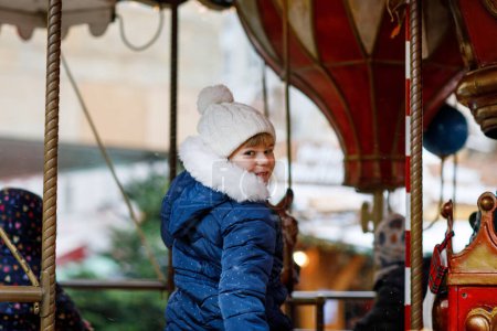 Foto de Niña preescolar montado en un alegre ir alrededor del carrusel caballo en la feria de Navidad o mercado, al aire libre. Feliz niño divirtiéndose en el tradicional mercado de Navidad familiar en Colonia, Alemania. - Imagen libre de derechos