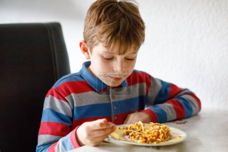 Photo for Cute healthy schoolkid boy eats pasta noodles sitting in school or nursery cafe. Happy child eating healthy organic and vegan food in restaurant or at home. Childhood, health concept. - Royalty Free Image