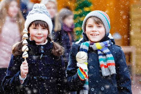 Photo for Little cute kid girl and boy eating white chocolate covered strawberries and apple on skewer on traditional German Christmas market. Happy children, best friends, twins and siblings on snowy day. - Royalty Free Image