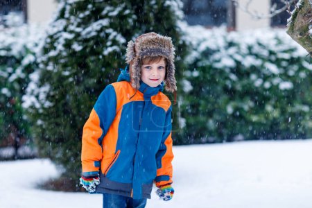 Photo for Funny little kid boy in colorful clothes playing outdoors during snowfall. Active leisure with children in winter on cold snowy days. Happy child having fun and playing with snow - Royalty Free Image