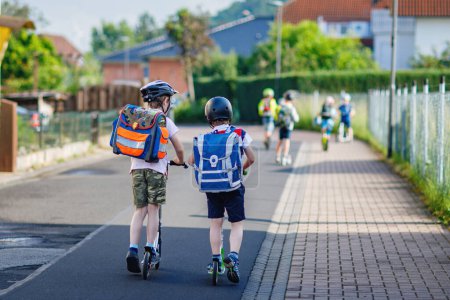 Photo for Two school kid boys in safety helmet riding with scooter in the city with backpack on sunny day. Happy children in colorful clothes biking on way to school. Safe way for kids outdoors to school. - Royalty Free Image
