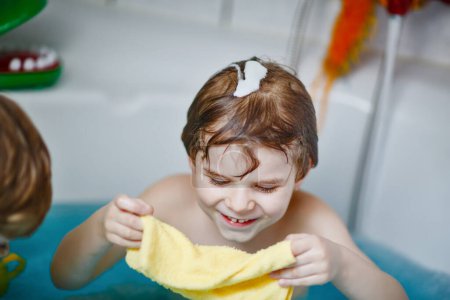 Photo for Cute little child playing with water by taking bath in bathtub at home. Adorable happy healthy preschool kid boy having fun, washing hairs and head and splashing with soap. - Royalty Free Image