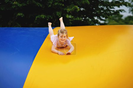 Foto de Una niña de preescolar saltando en el trampolín. Feliz niño divertido que se divierte con la actividad al aire libre en verano. Deportes y ejercicios para niños. Trampolín en colores de bandera ucraniana. - Imagen libre de derechos